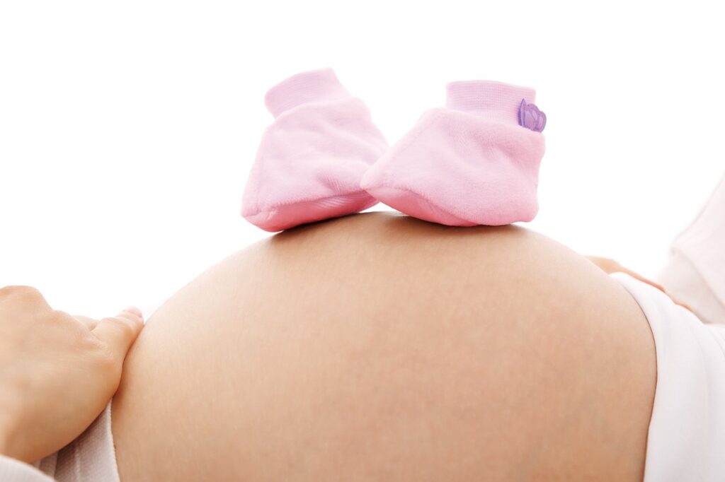 Der Bauch einer schwangeren Frau mit Babyschuhen drauf