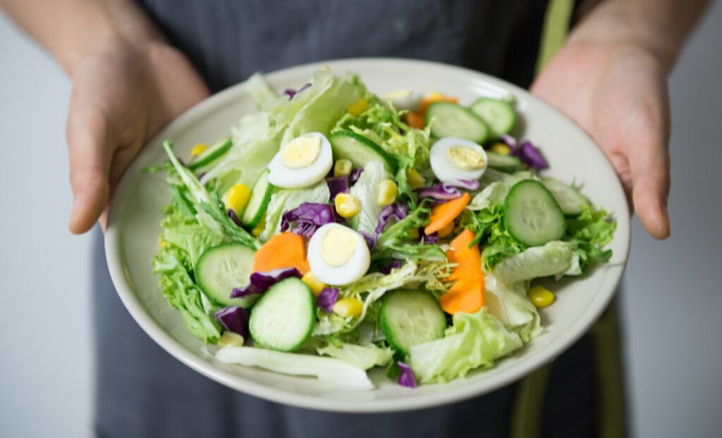 Grüner Salat in einer großen Schüssel, gehalten von einem Menschen