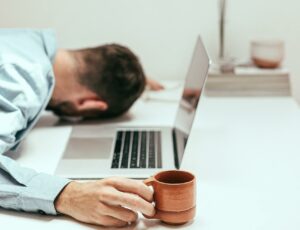 Mann mit Laptop schläft mit dem Kopf auf dem Schreibtisch