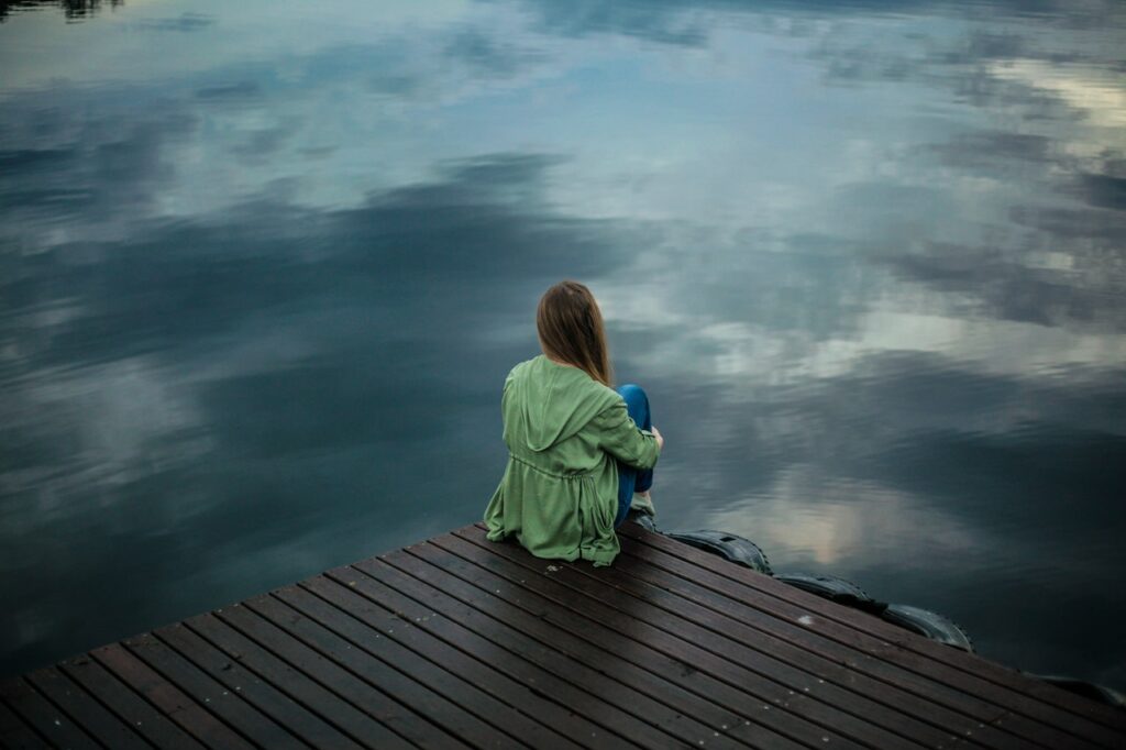 Frau sitzt auf einem Steg am Wasser